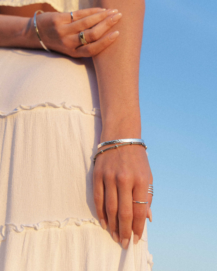 Close-up of a person's hands wearing multiple rings and bracelets against a clear blue sky.